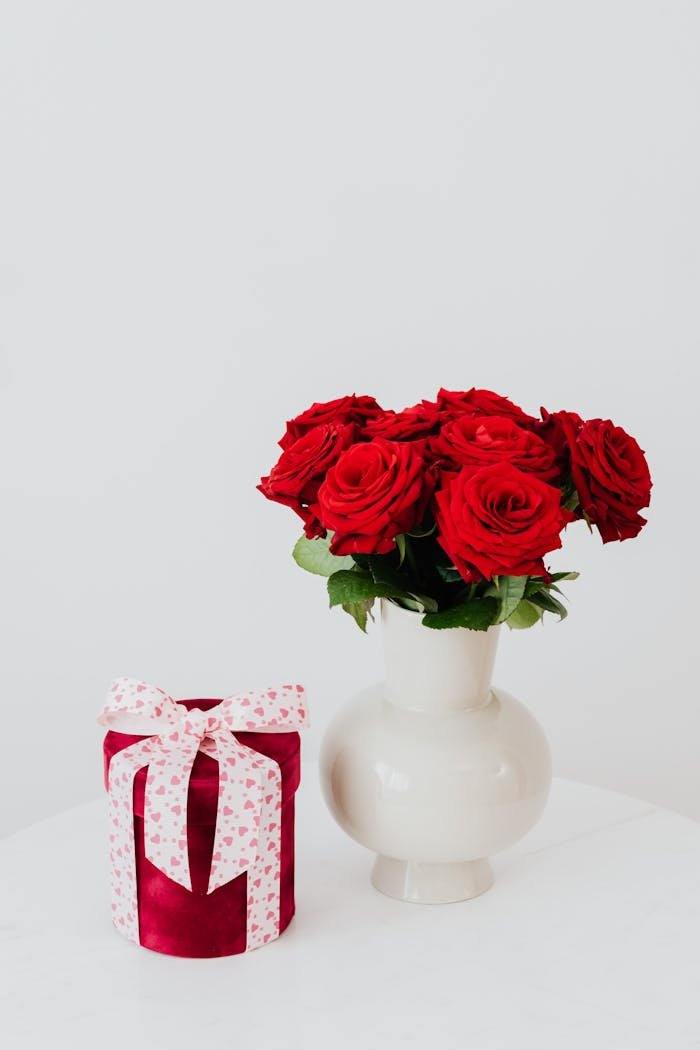 Beautiful bouquet of red roses in a vase beside a wrapped gift, perfect for romantic occasions.